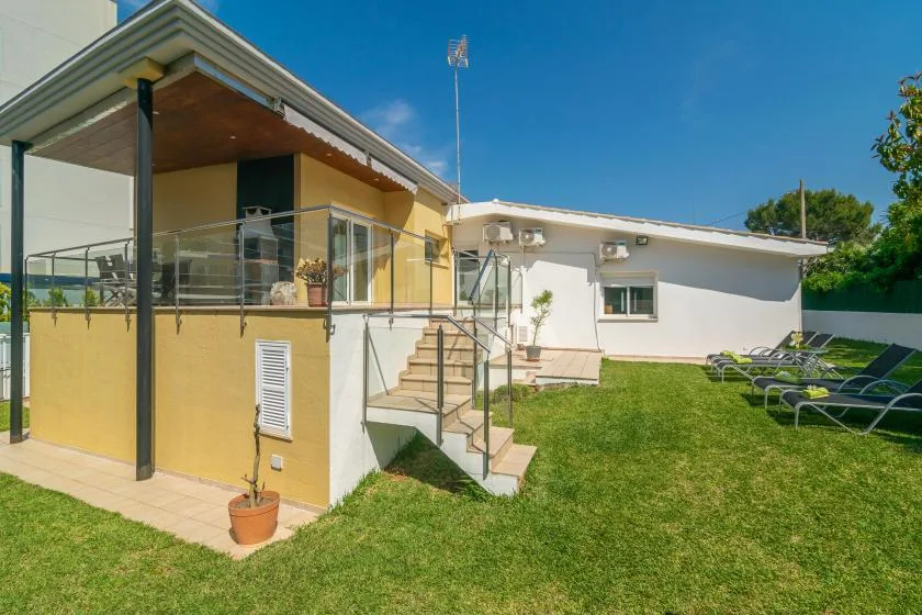 Una casa moderna da a un jardín con césped y tumbonas.