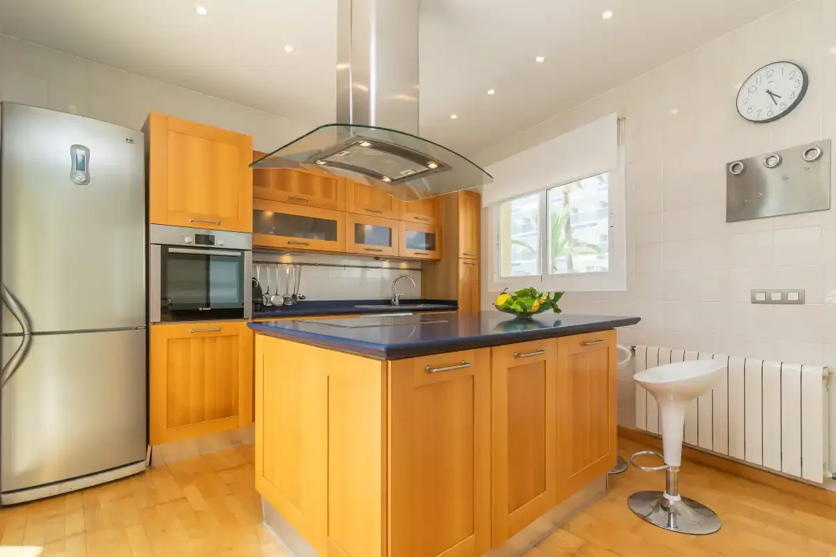 Una cocina luminosa con gabinetes de madera, una isla central y electrodomésticos de acero inoxidable.