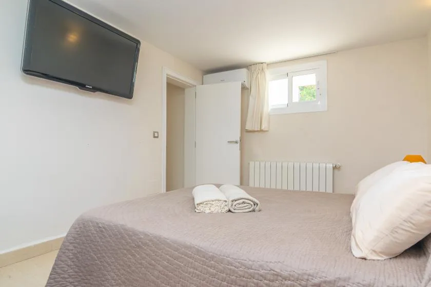 Un dormitorio con una cama, un televisor montado en la pared y una ventana pequeña.