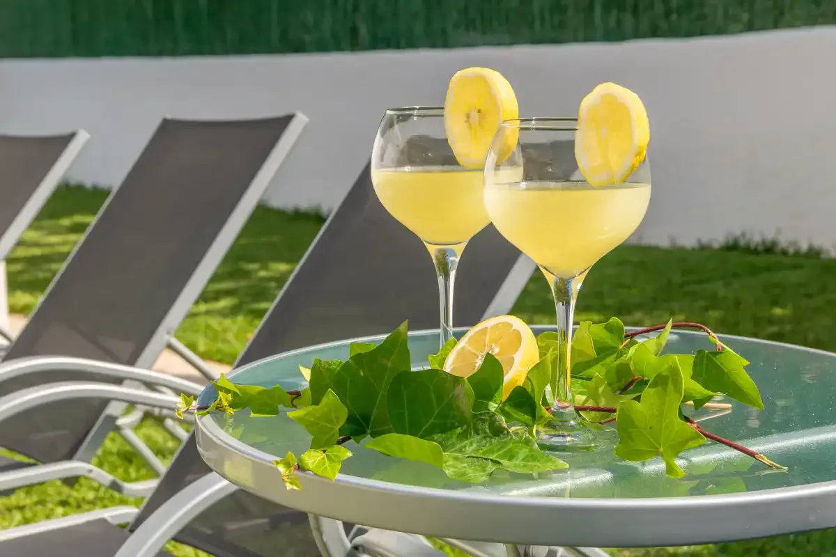 Asientos en un patio exterior junto a una mesa de vidrio con dos bebidas adornadas con limón.