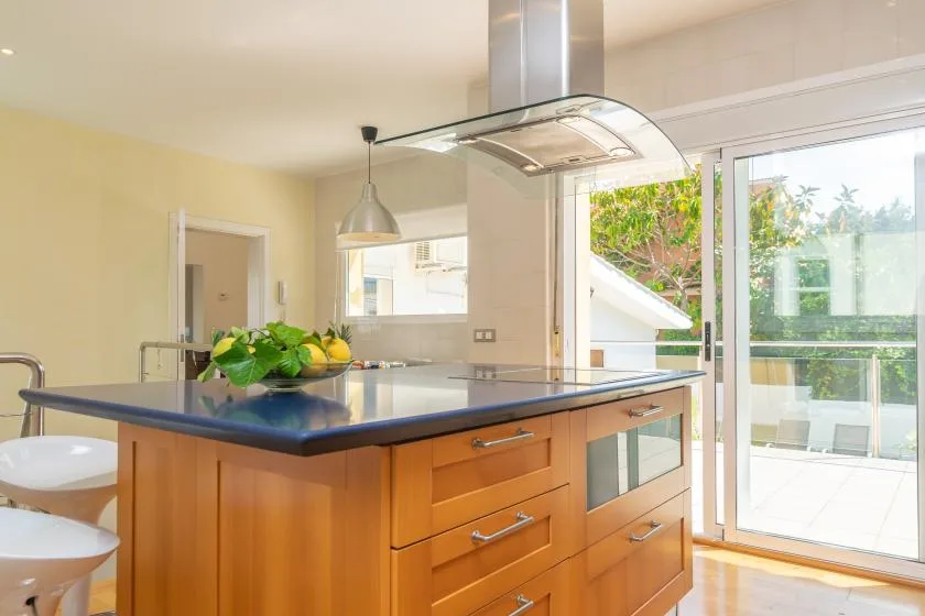 Cocina con una isla central, campana extractora y grandes puertas de vidrio.
