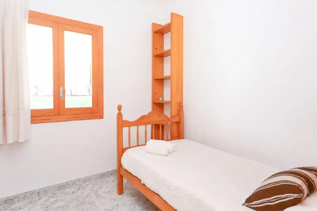 Un dormitorio con una cama individual junto a una ventana y estantes de madera.