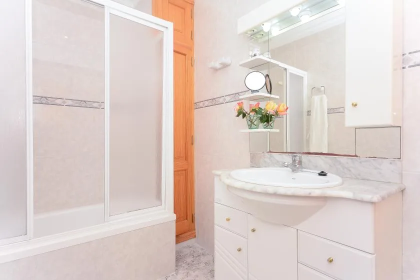 Un baño luminoso con lavabo y una mampara de ducha de vidrio.