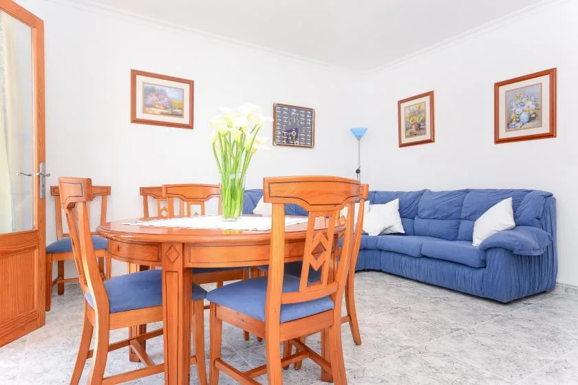 Un comedor con asientos de madera junto a un sofá azul y cuadros enmarcados.