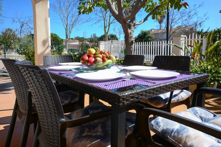 Una mesa de comedor al aire libre está puesta con platos bajo un árbol frondoso.
