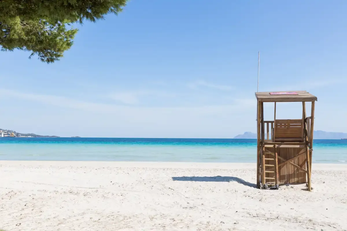 Una playa de arena con agua turquesa y una torre de vigilancia de madera.
