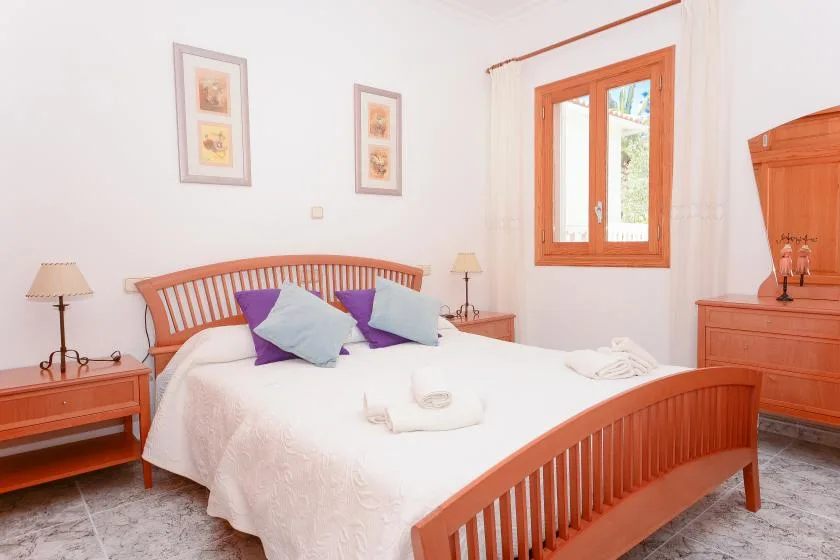 Un dormitorio con cama de madera, ropa de cama blanca y una ventana con cortinas.