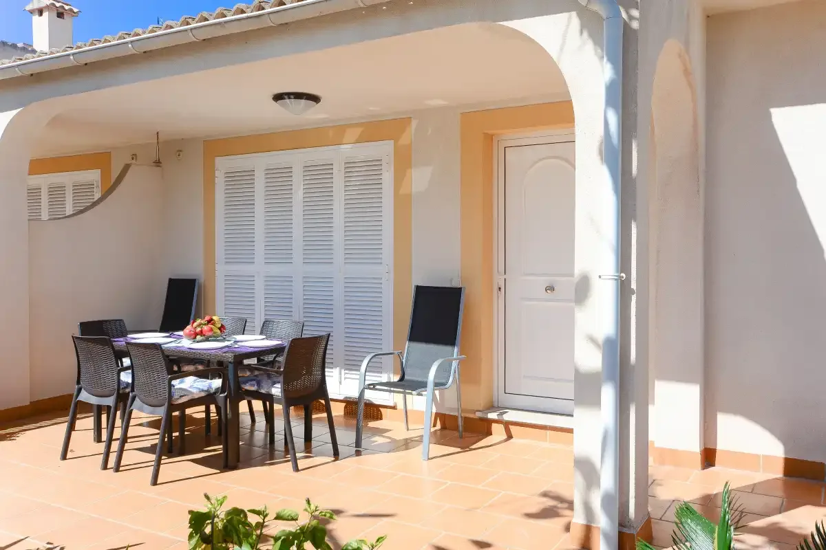 Un patio cubierto con asientos y una mesa junto a puertas con contraventanas.