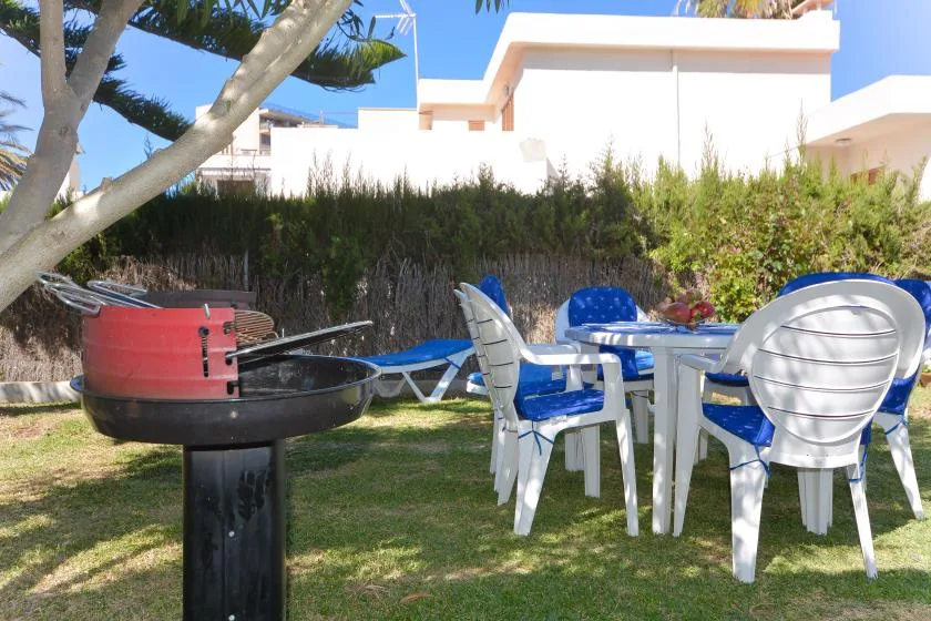 Un patio al aire libre con una parrilla, asientos de plástico y una mesa sobre el césped.