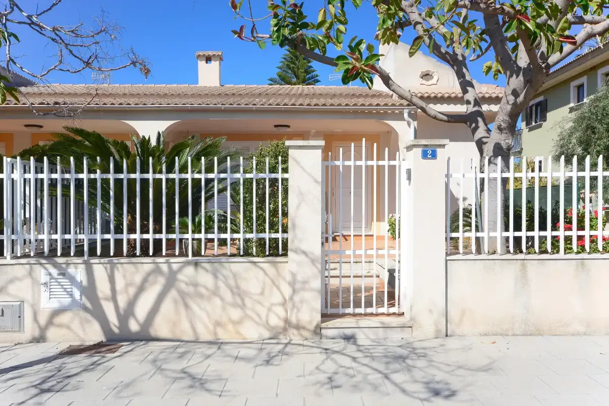 La fachada de una casa con una verja y una puerta metálicas blancas.