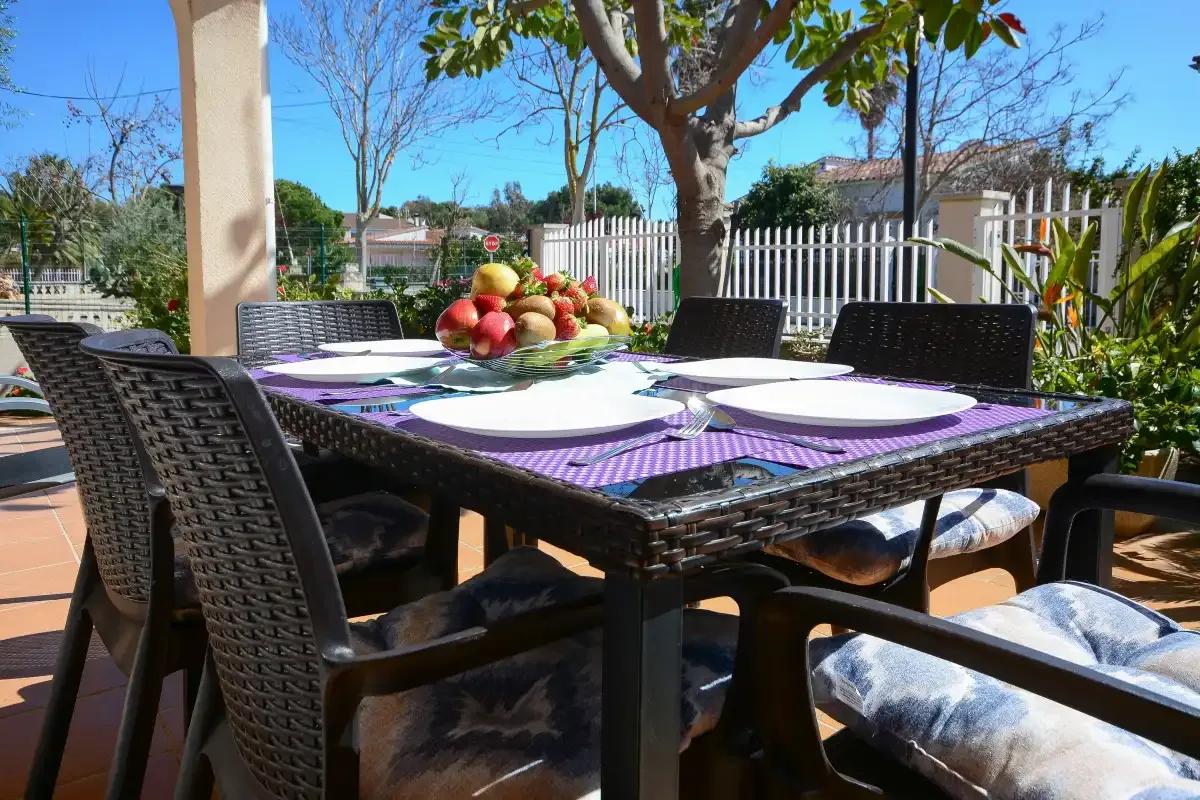 Una mesa de comedor al aire libre está puesta con platos y fruta junto a un jardín.