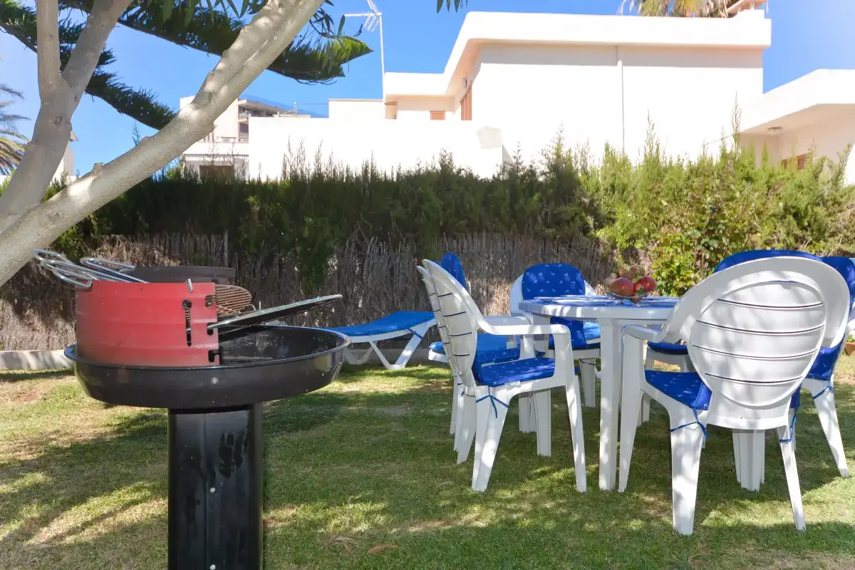 Comedor al aire libre con asientos de plástico y una barbacoa en un jardín.