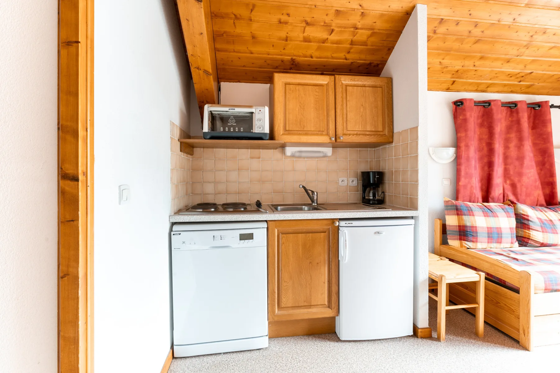 A compact kitchen with wooden cabinets and appliances beneath a wood-paneled ceiling.