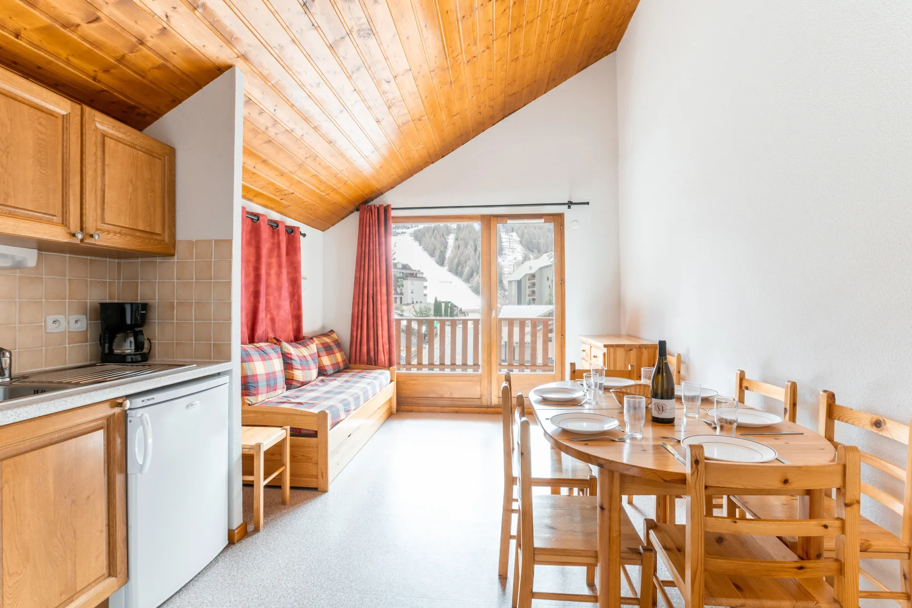 A bright dining area with a wooden table beside a compact kitchen and seating nook.
