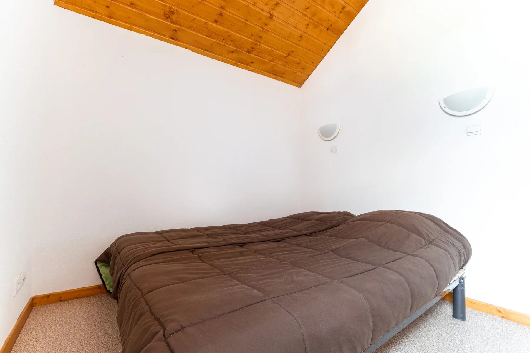 A bedroom with a bed beneath a sloped wooden ceiling.
