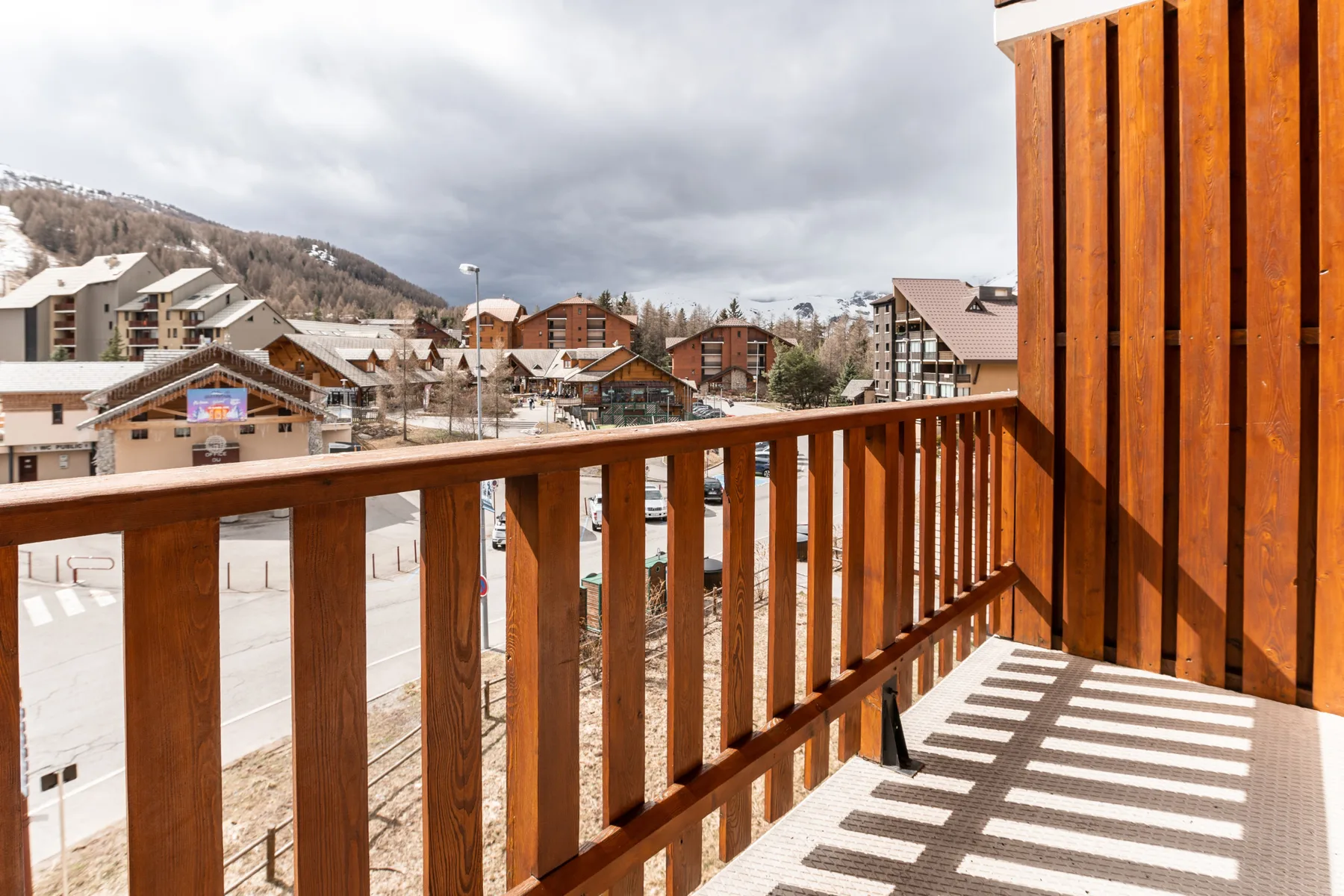 A balcony overlooks a mountain village, with wooden railings in the foreground.