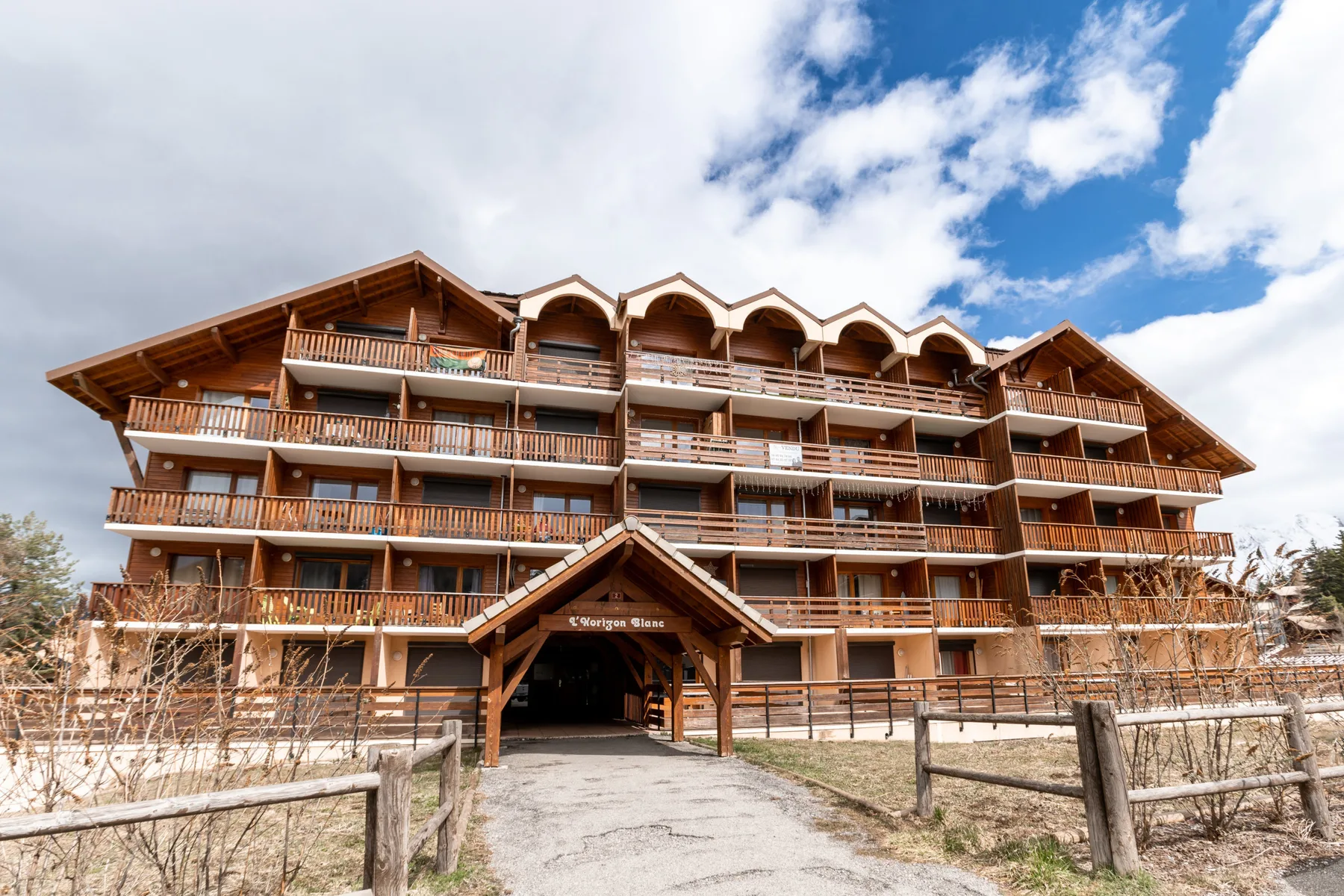 A multi-story building with wooden balconies stands beneath a partly cloudy sky.