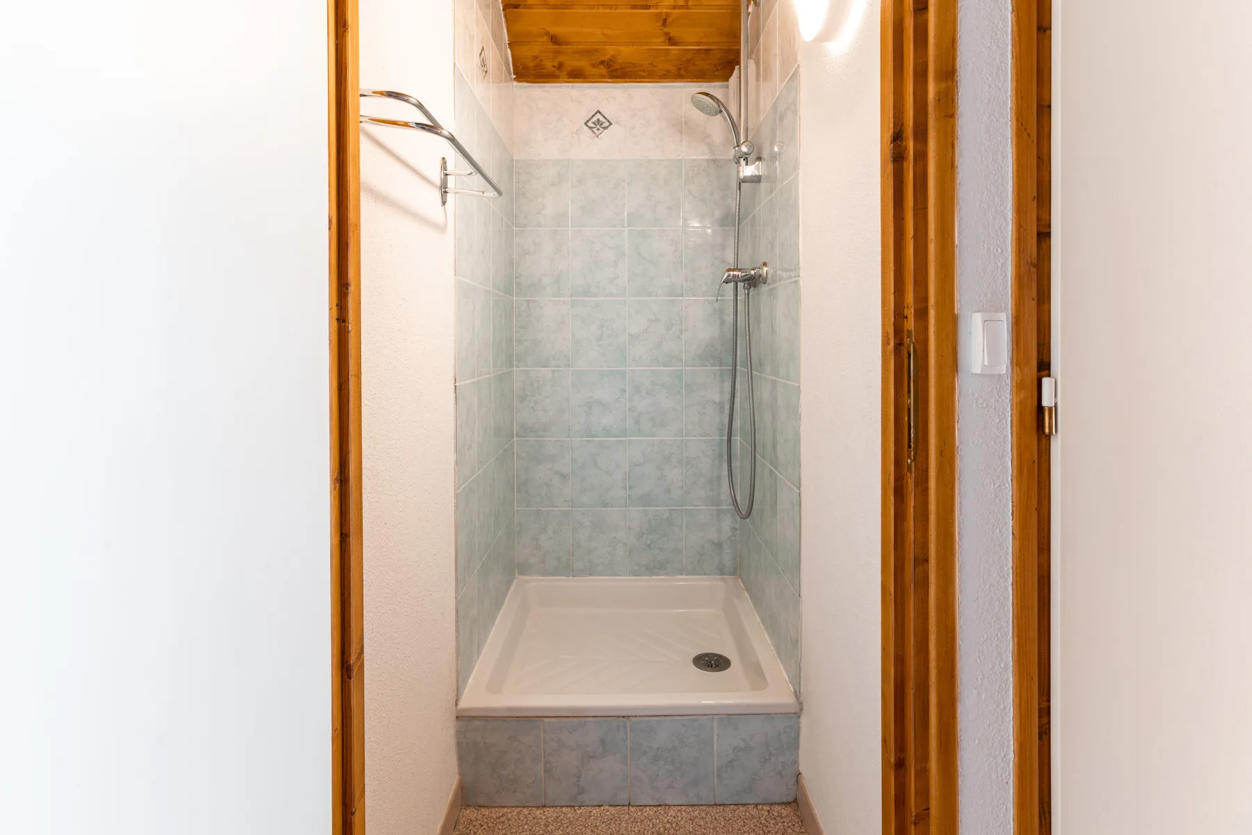 A tiled shower with a handheld showerhead and a wooden ceiling.