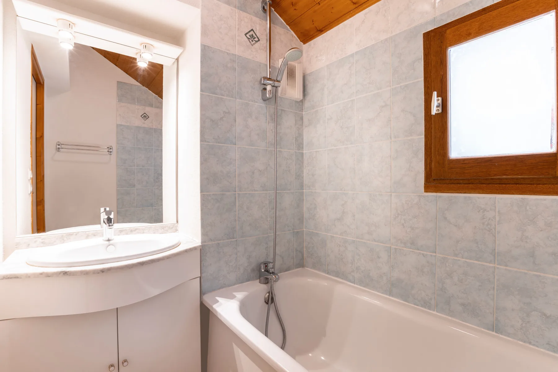 A tiled bathroom with a bathtub, shower, and window.