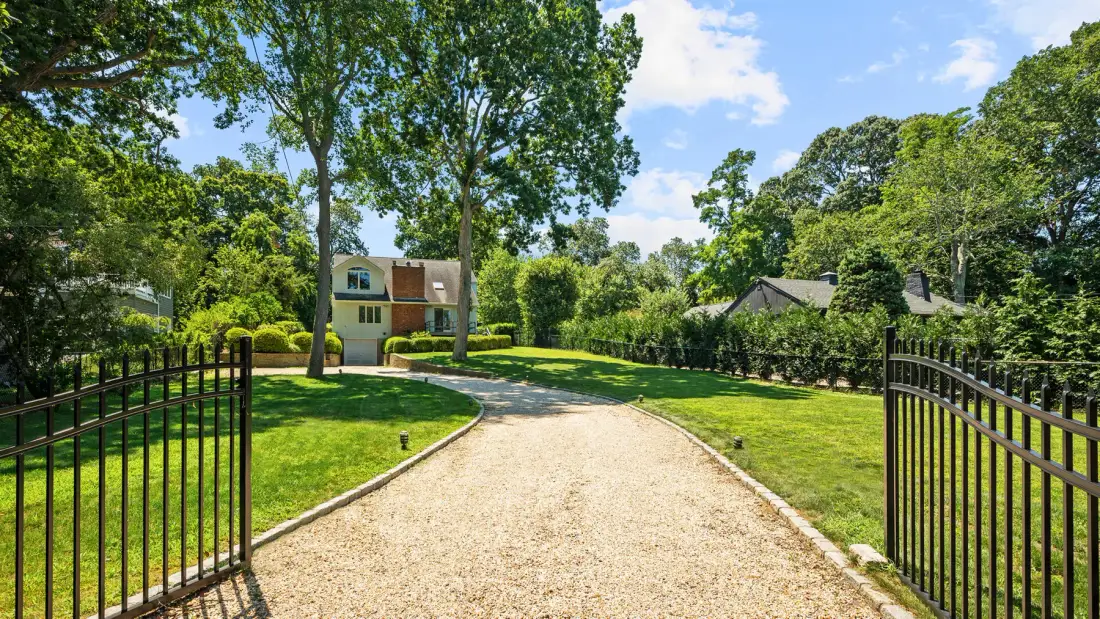 A gravel driveway curves through a green yard between open gates.