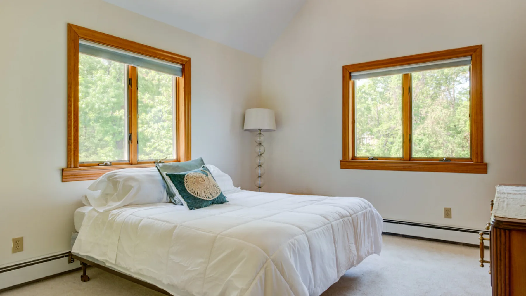 Un dormitorio con una cama bajo dos ventanas con marcos de madera.