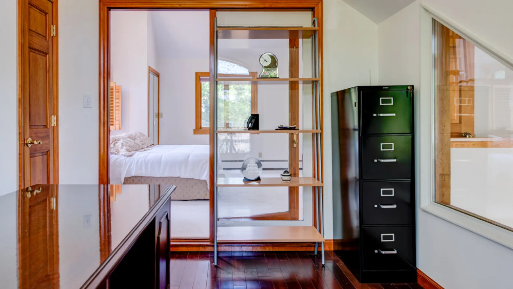Se ve un dormitorio a través de una división de madera, junto a un escritorio y un archivador.