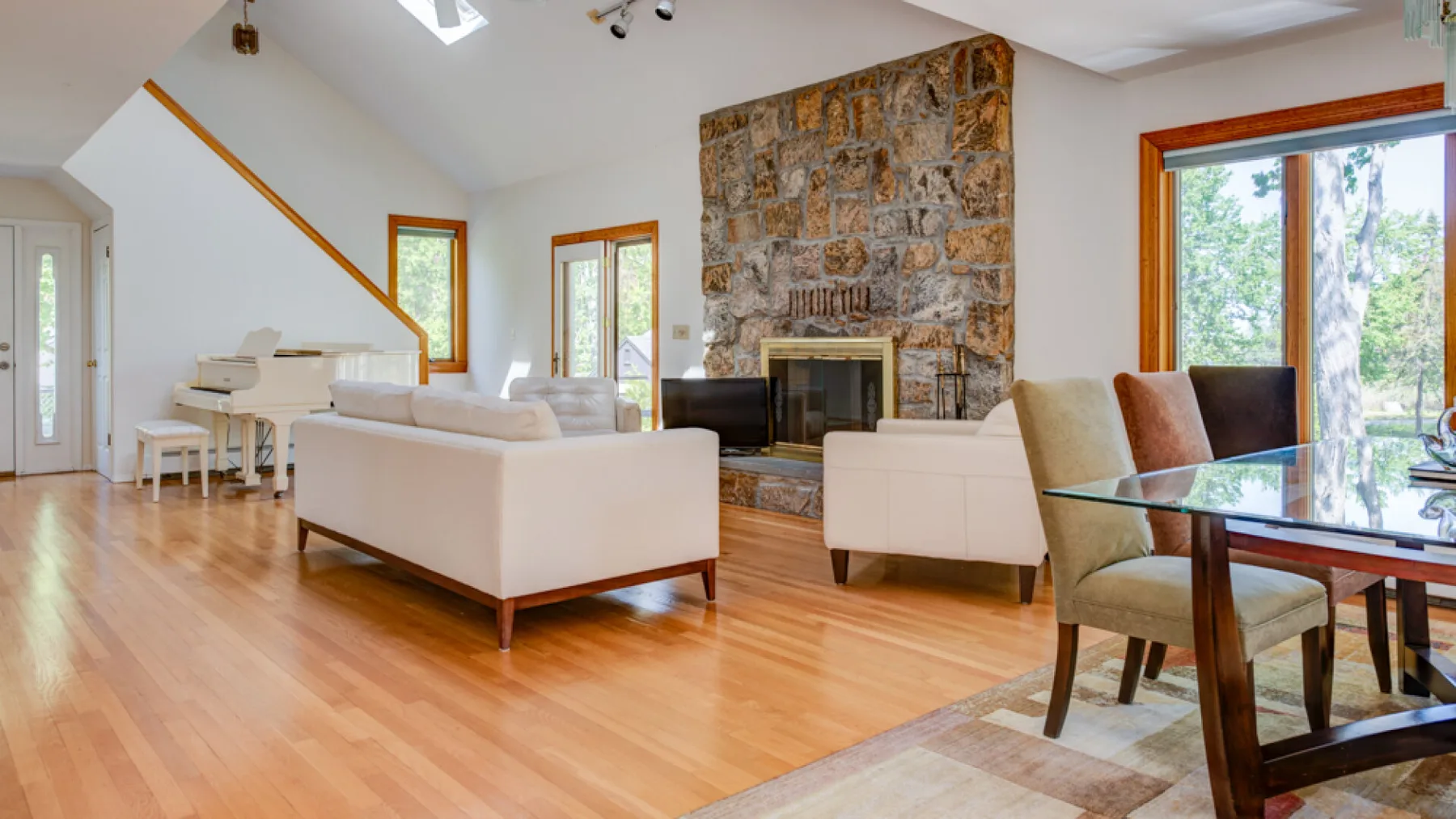 A bright living room with seating, a stone fireplace, and a dining table.
