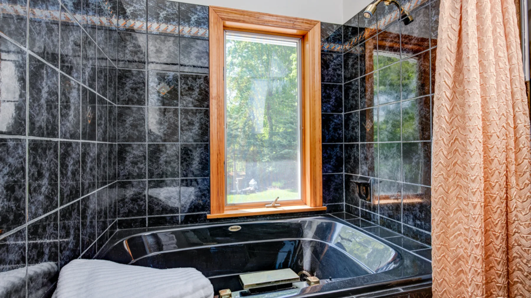 Un baño con una bañera esquinera negra bajo una ventana.