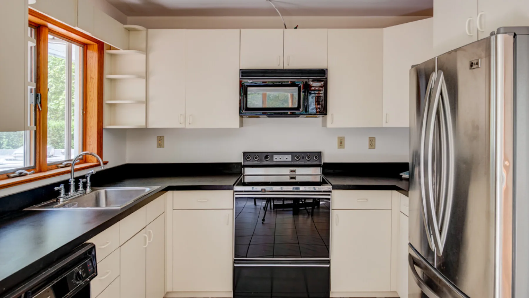 Una cocina con gabinetes blancos, encimeras oscuras y electrodomésticos de acero inoxidable.