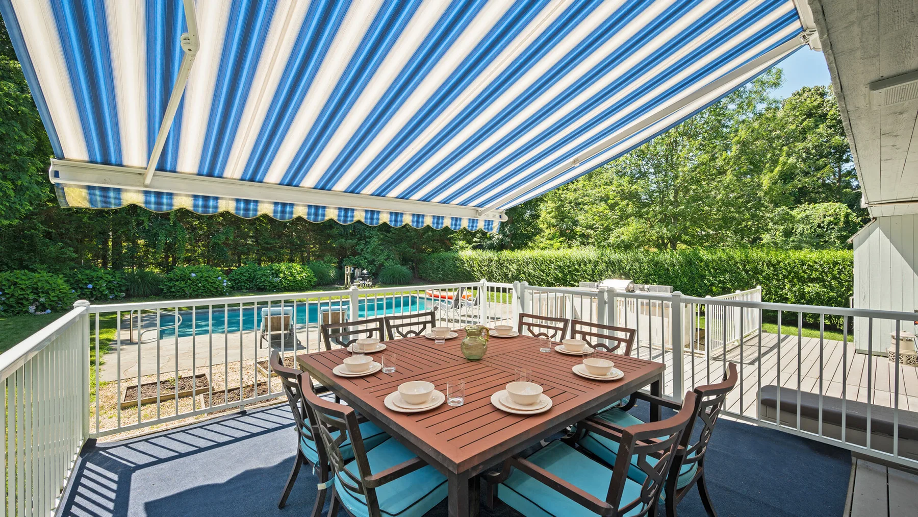 Una zona de comedor al aire libre está bajo un toldo a rayas, junto a una piscina.