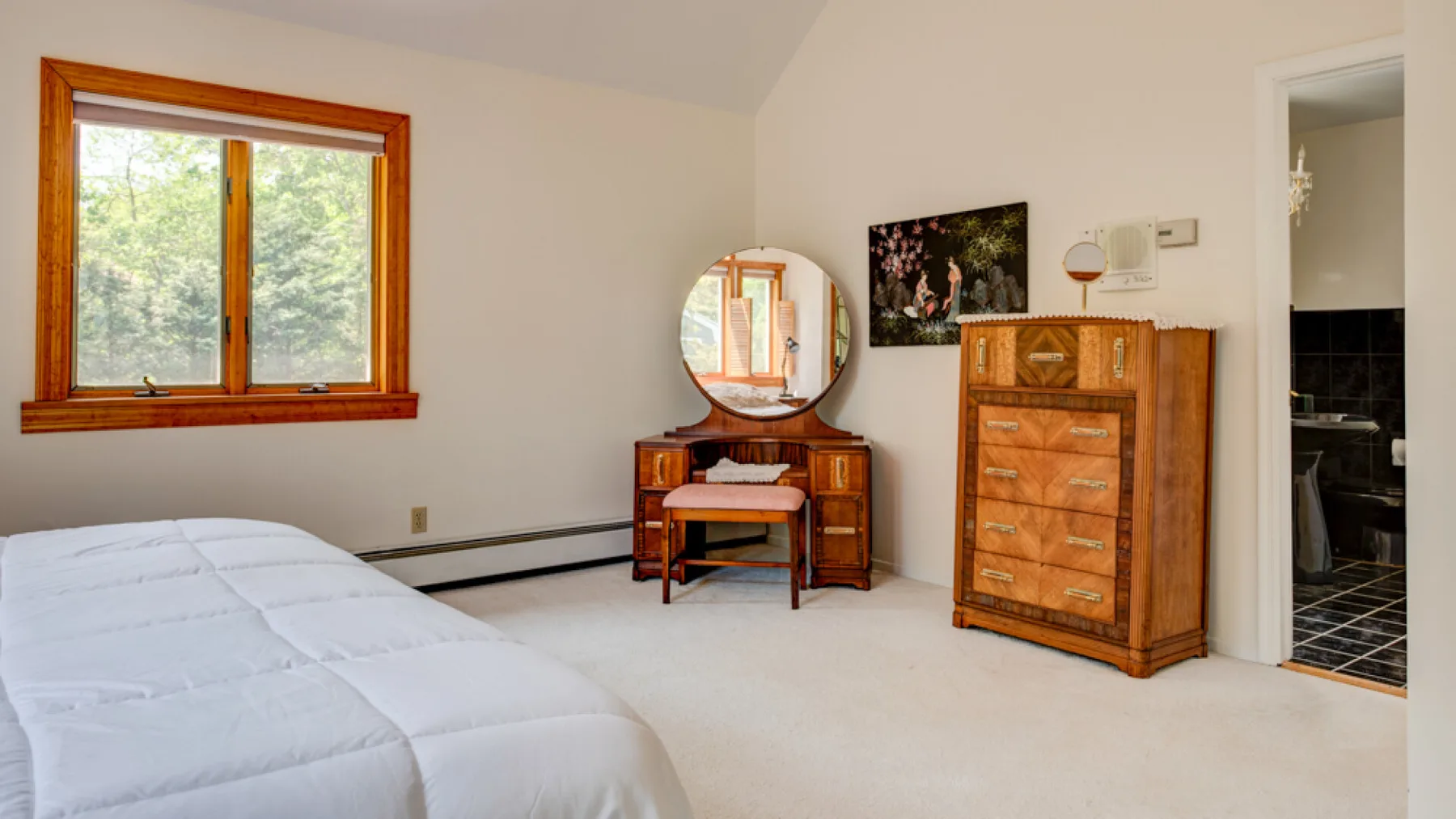 Un dormitorio con una cama, cómodas de madera y una ventana con vista a los árboles.