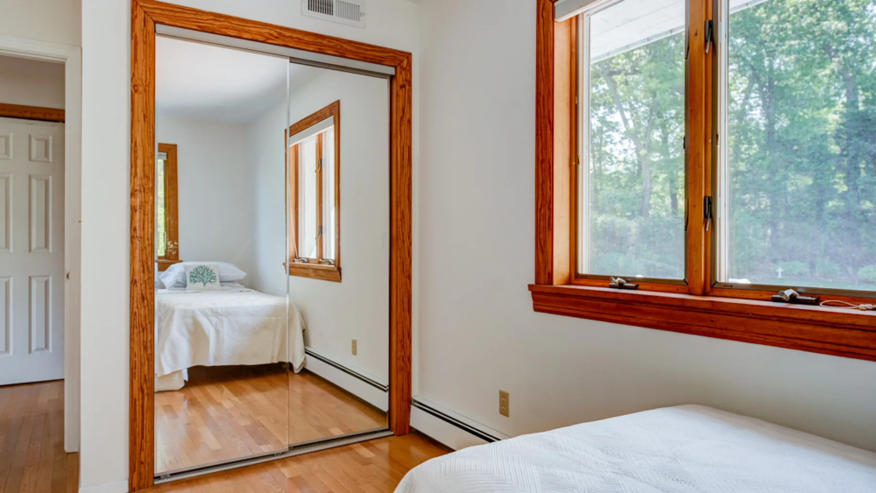 Un dormitorio con una cama junto a una ventana grande con árboles frondosos a la vista.