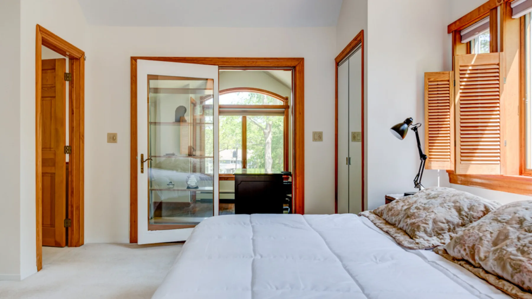 Un dormitorio con una cama junto a una ventana con contraventanas de madera.