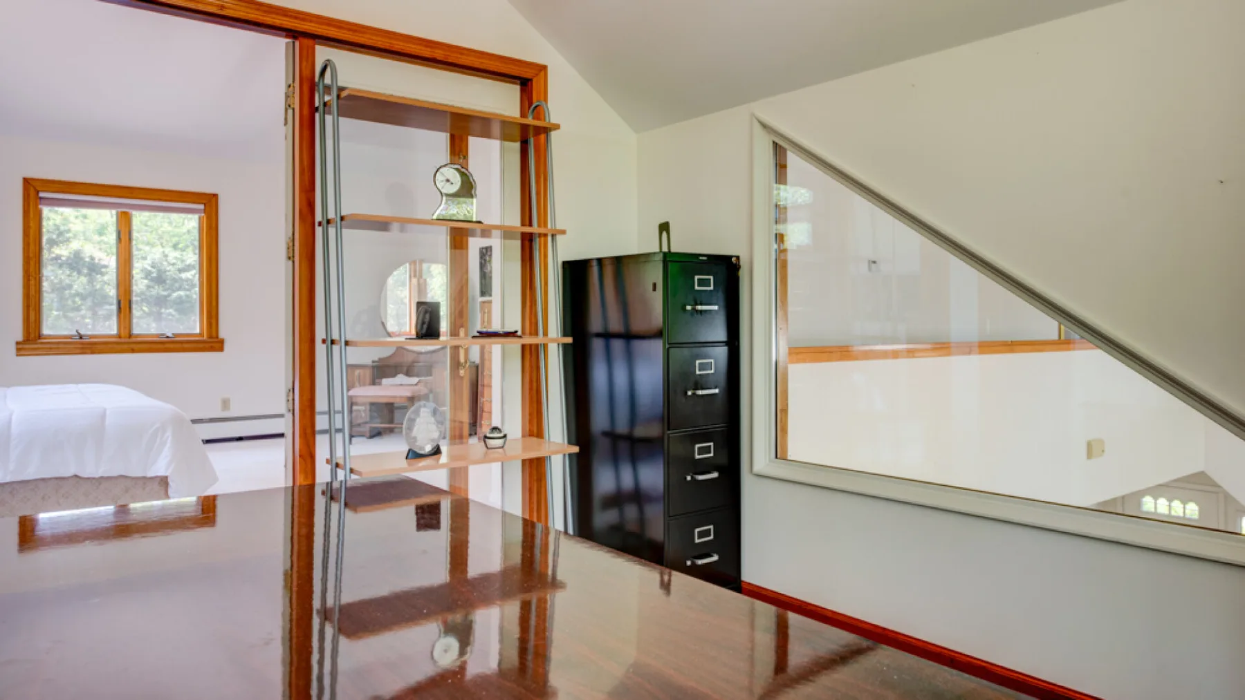 Una habitación luminosa con una cama, una vitrina de cristal y un archivador.