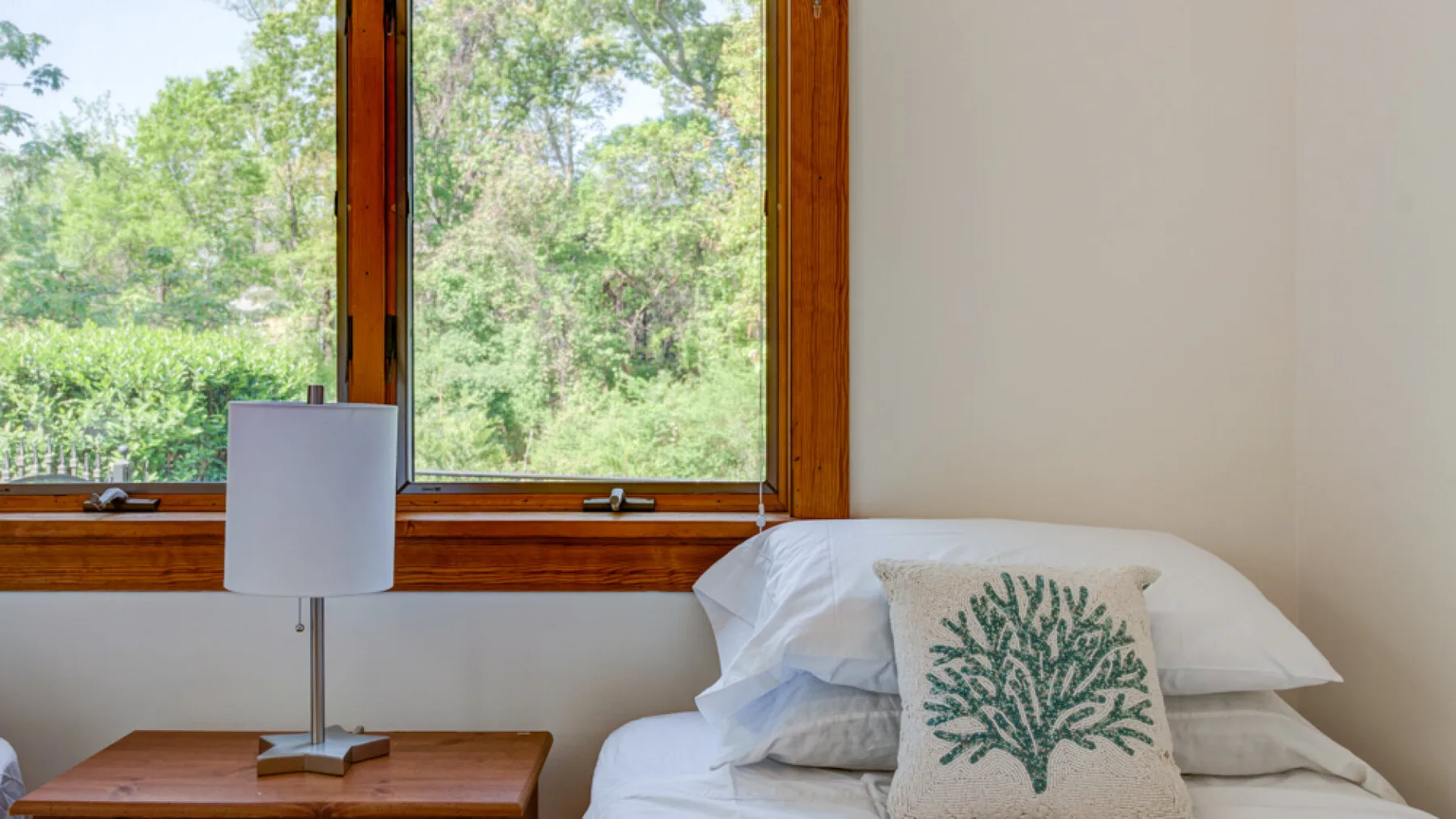 Un dormitorio con una cama junto a una ventana grande con vistas a la vegetación.
