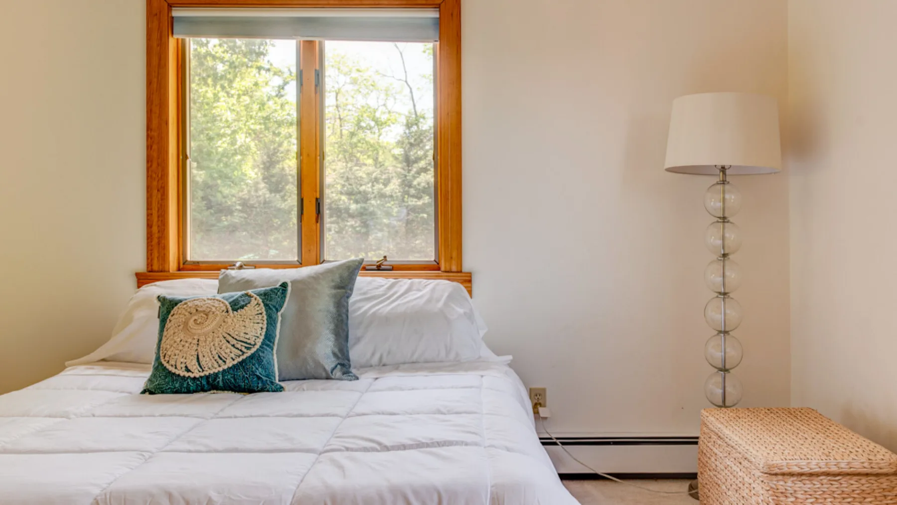 Un dormitorio con una cama, cojines decorativos y una ventana con vistas a árboles.