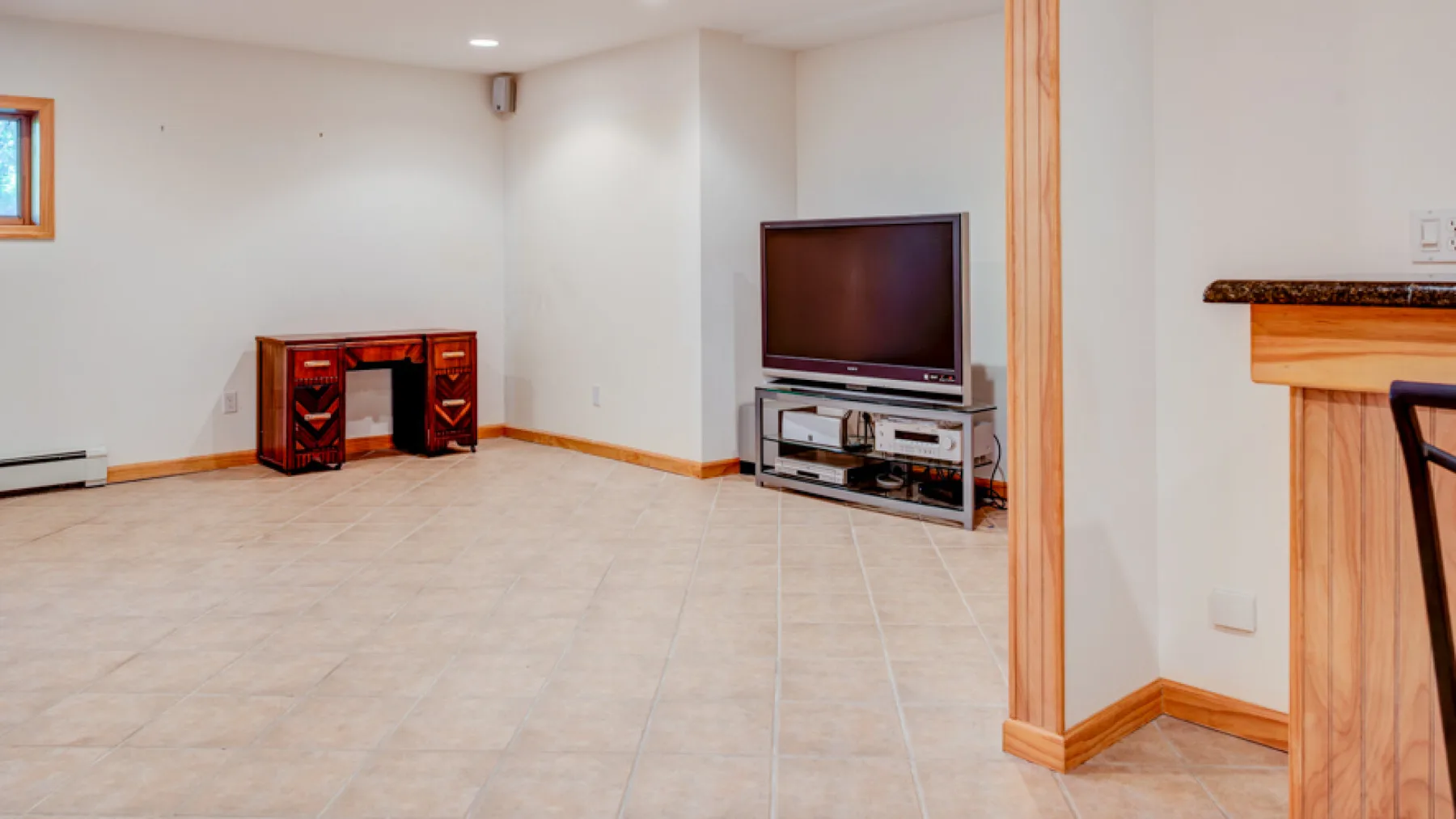 Una sala amplia con suelo de baldosas, un televisor y una mesa pequeña.