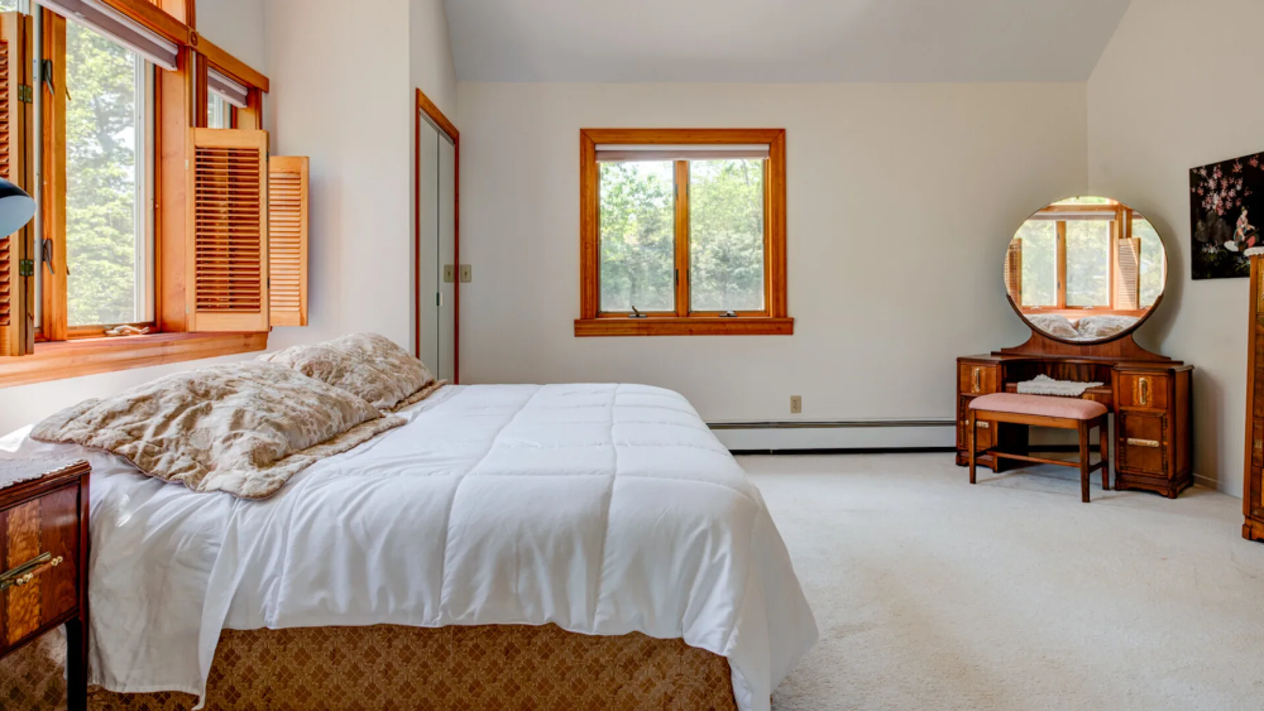 Un dormitorio luminoso con una cama bajo ventanas con marcos de madera.
