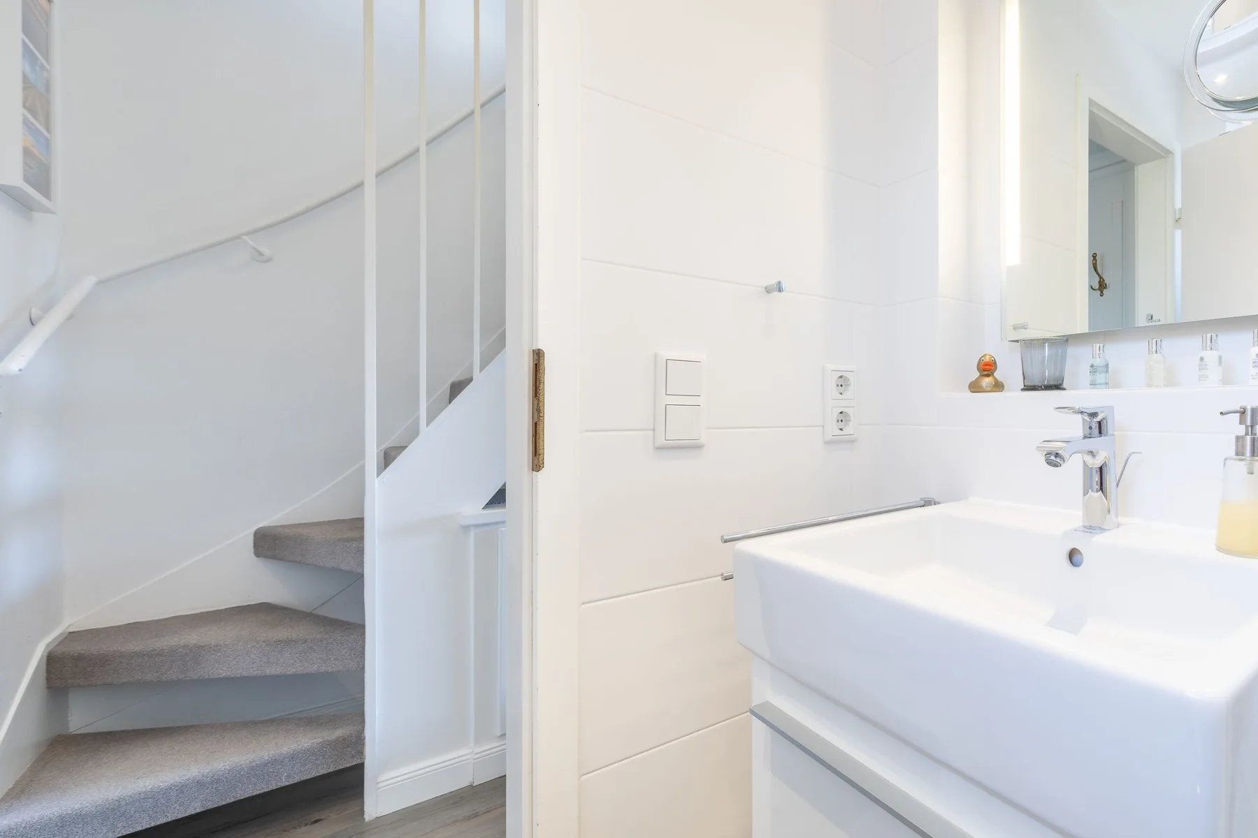 A bright bathroom with a white sink beside a staircase.