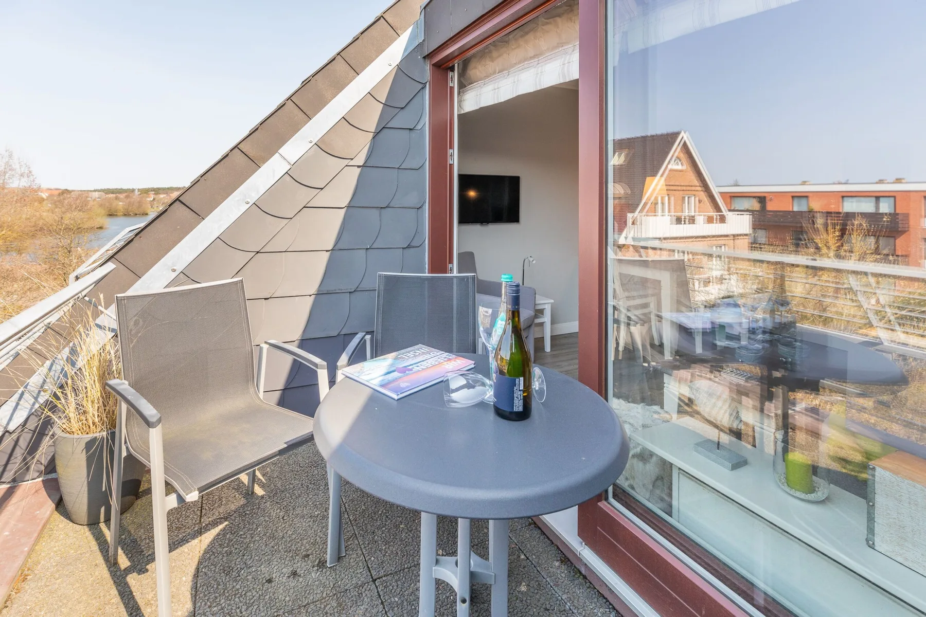 A small balcony with outdoor seating and a round table beside glass doors.