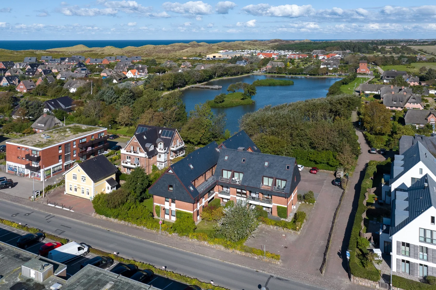 An aerial view of a residential neighborhood with a pond and the sea in the distance.