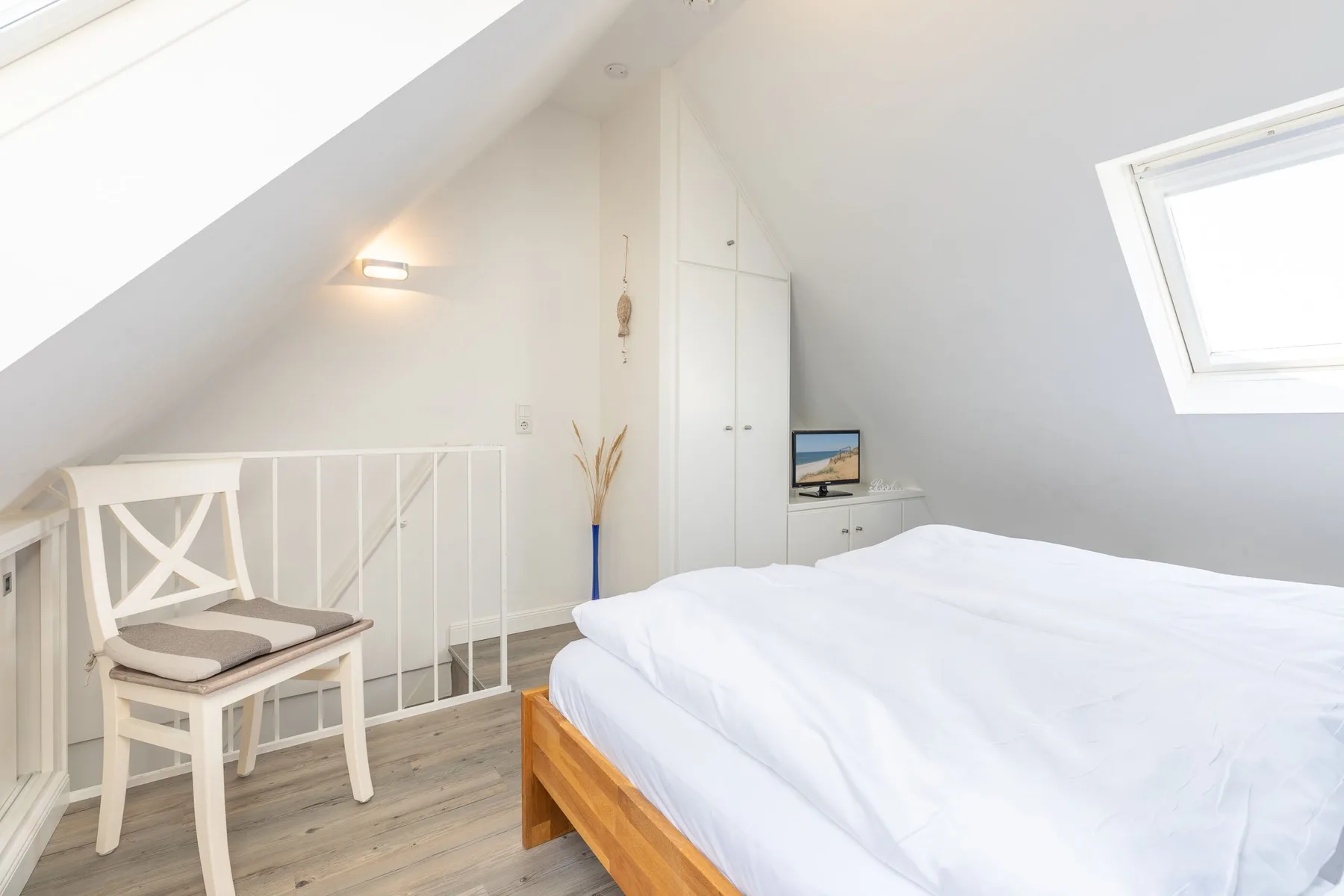 A bright attic bedroom with a bed, a chair, and a skylight.