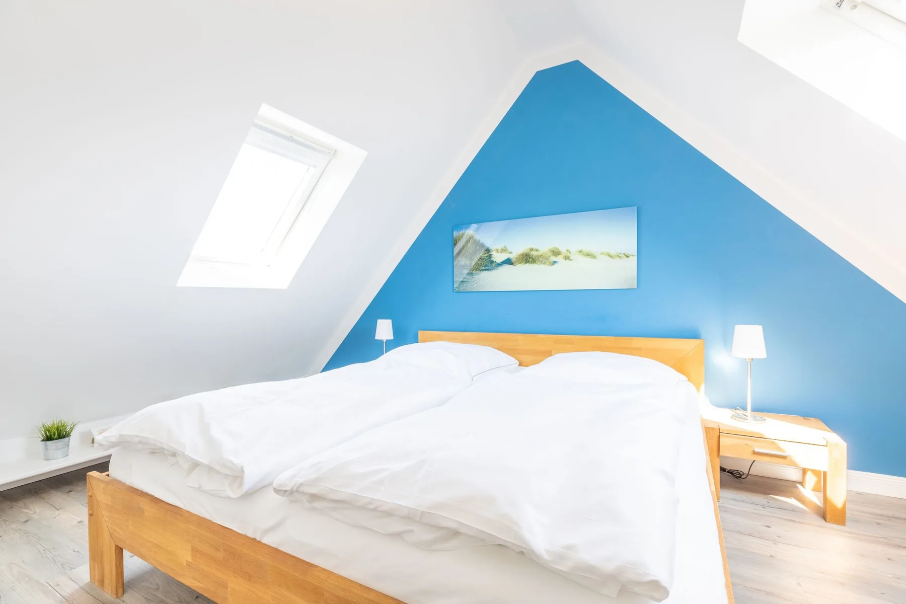 A bright bedroom with a bed against a blue accent wall.