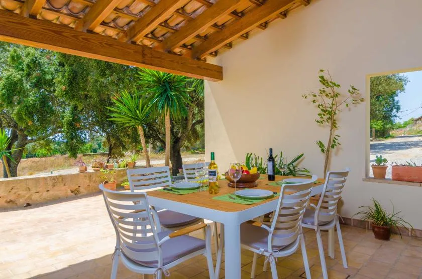 A covered outdoor dining area with a table set beneath a wooden roof.