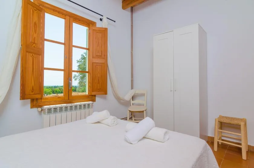 A bedroom with a bed, towels, and a window overlooking greenery.