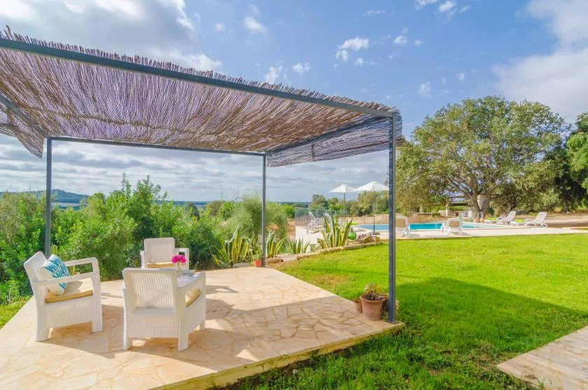 A shaded outdoor seating area overlooks a lawn, trees, and a swimming pool.