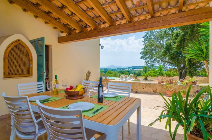 A covered outdoor dining area with a wooden table and chairs overlooks a leafy landscape.