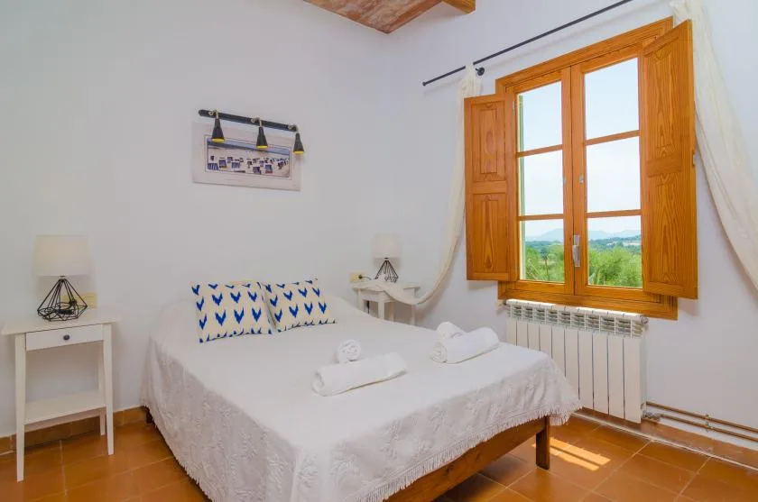 A bright bedroom with a bed beneath a wooden-framed window.