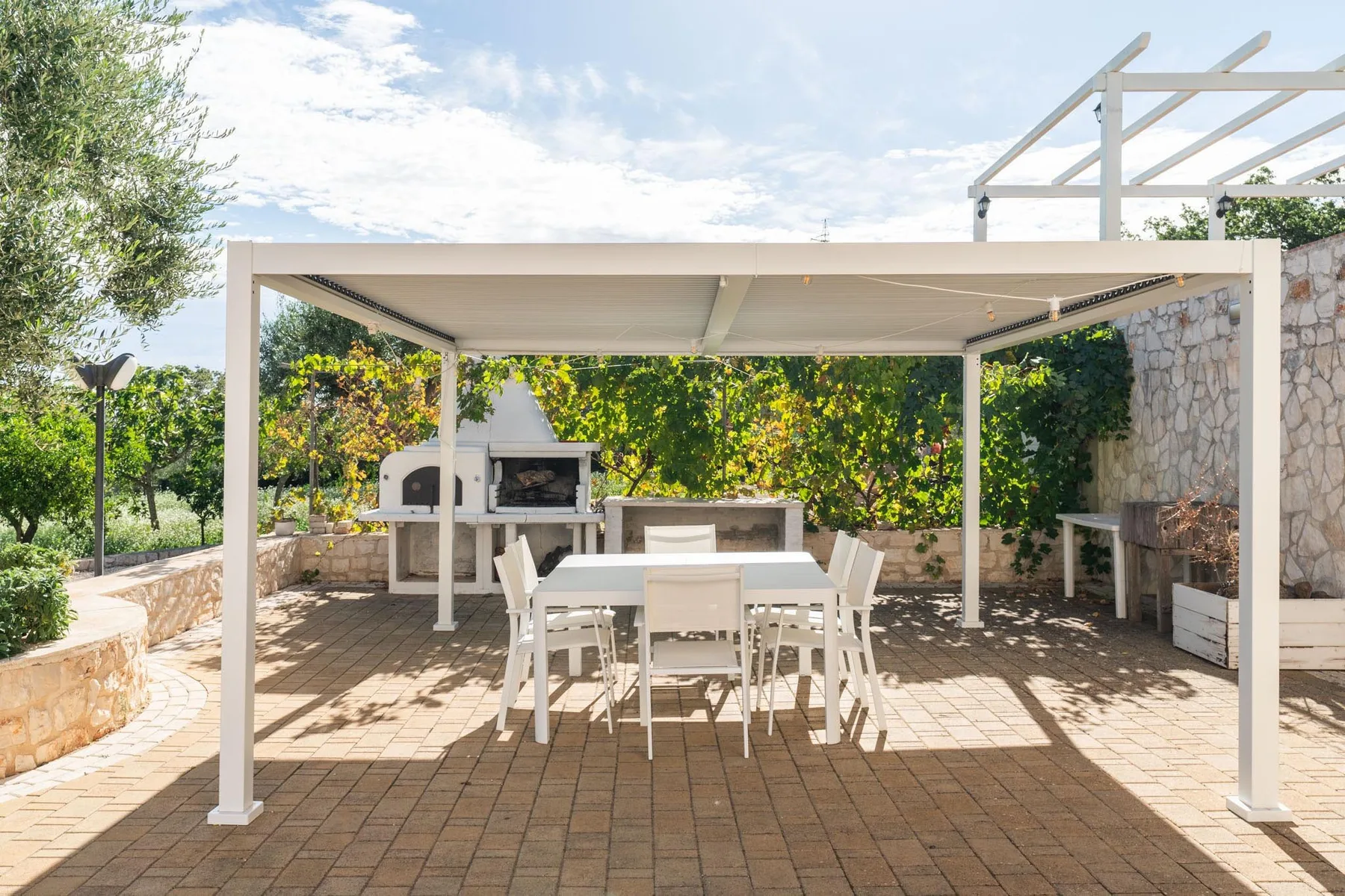 Un comedor al aire libre bajo una pérgola, con mesa y asientos.