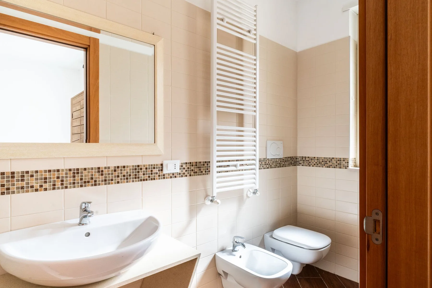Un baño alicatado con lavabo, inodoro y radiador toallero de pared.